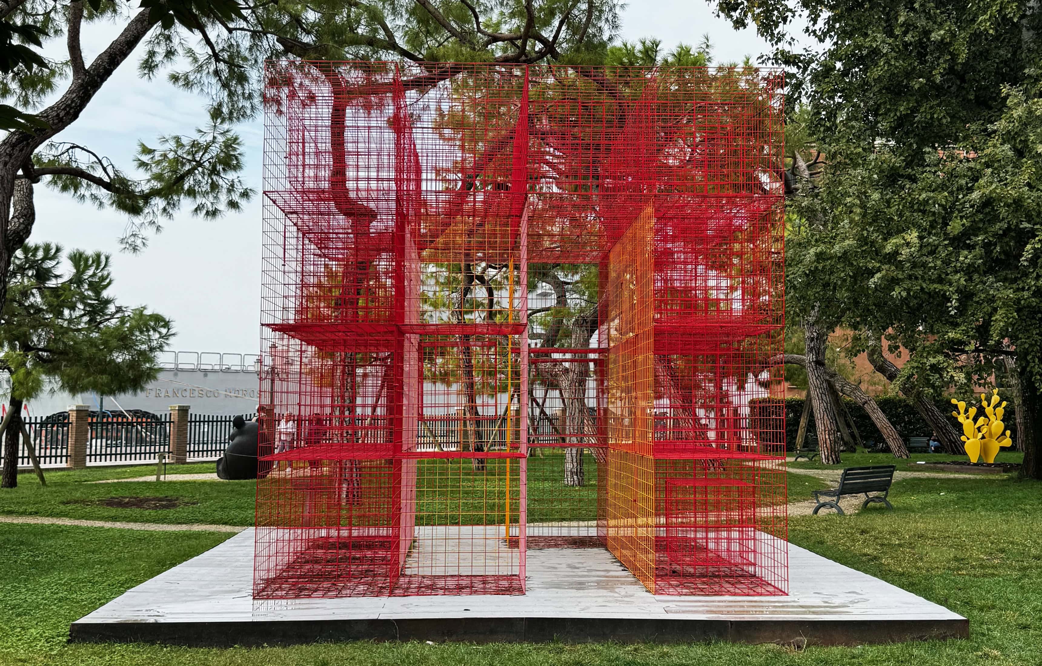 A red steel mesh house standing in the Giardini della Marinaressa with the Venice lagoon behind